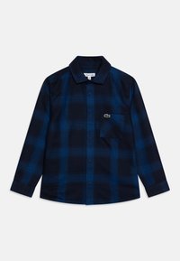 Camicia a quadri blu navy con bottoni, realizzata in flanella, dotata di una tasca sul petto e di un piccolo logo di coccodrillo verde sulla tasca.