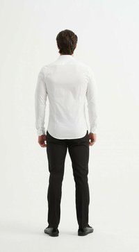 Chemise blanche à manches longues avec un ourlet arrondi, associée à un pantalon noir et des chaussures noires. La chemise présente une texture de tissu lisse.