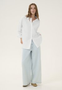 White button-up shirt with long sleeves, paired with light blue wide-leg jeans and beige shoes. Simple, relaxed fit, smooth fabric texture.