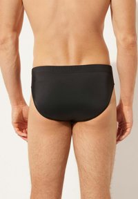 Schwarze Schwimmbeinkleider mit glatter Textur, niedrigem Schnitt und einem schlichten, klaren Design. Mit elastischem Bund ohne zusätzliche Akzente.