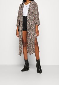 Blommig kimono med svart bakgrund, prydd med livfulla flerfärgade blommor, långa ärmar och höga sidoklyftor. Matchad med svarta shorts och stövlar.