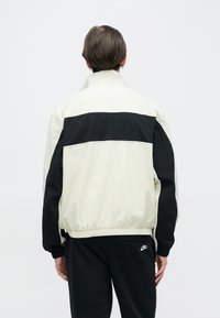 Ελαφρύ μπουφάν με κρεμ σώμα και μαύρη οριζόντια ρίγα, ελαστικά μανίκια και ψηλό γιακά. Υφή υφάσματος, χαλαρή εφαρμογή.