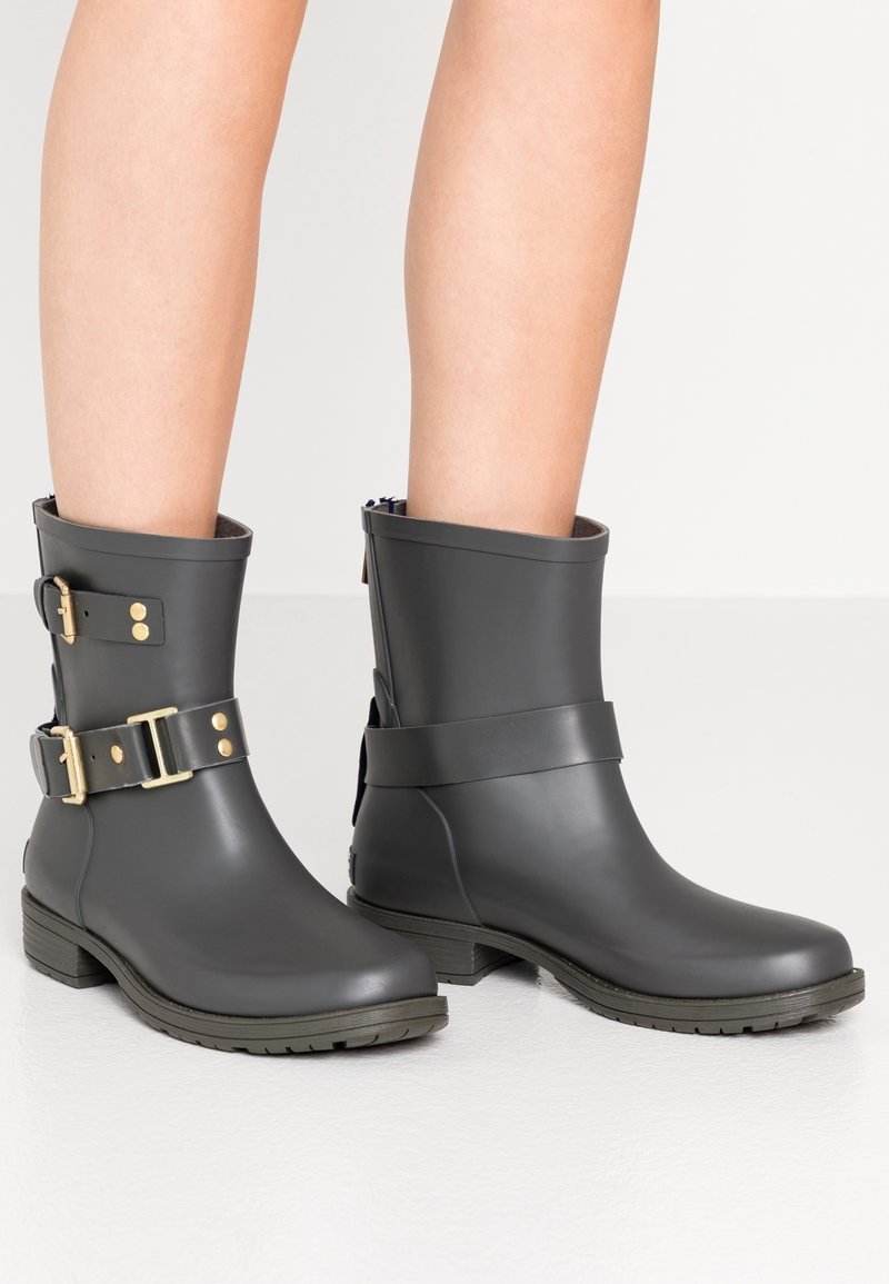 Bottes de cheville en caoutchouc gris avec des boucles et des accents dorés, semelle texturée et finition lisse. Comprend une couleur intérieure contrastante et un design épuré.