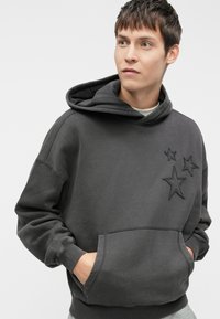 Sweatshirt cinza escuro com um bolso canguru, apresentando três estrelas bordadas no peito, e um tecido macio e texturizado.