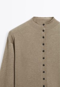 Cardigan en maille brun clair avec un col rond et une rangée verticale de boutons noirs sur le devant.
