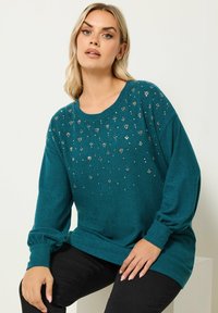 Sweatshirt long à manches en teal avec un col arrondi et des détails embellis comportant de petites accents métalliques et gemmés. Coupe décontractée.