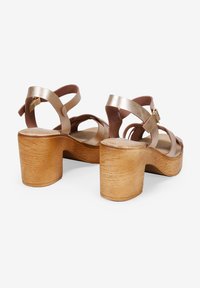 Brown leather platform sandals with crossed straps and adjustable buckle. Block heel with a wood texture. Smooth, shiny finish on straps.