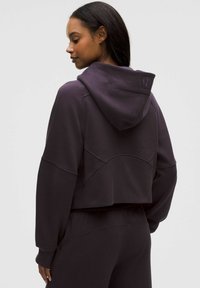 Gekürzter Kapuzenpullover in dunklem Lila, mit strukturiertem Stoff, weiten Ärmeln und einem gestickten Logo auf der Rückseite.