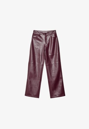 Osoba ubrana w szary sweter z odkrytymi ramionami, wysokie burgundowe skórzane spodnie oraz czarne szpilki, trzymająca dużą czarną kopertówkę.