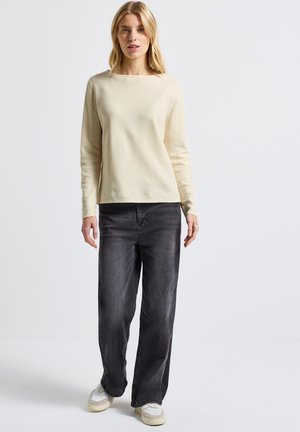 Sweater beige clair à manches longues avec texture côtelée, associé à un jean large taille haute gris foncé et des baskets blanches décontractées.
