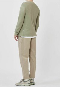 Vaaleanvihreä ribbineulottu pitkähihainen paita, beiget löysät housut ja harmaat lenkkitossut vihreillä yksityiskohdilla. Yksinkertainen muotoilu ilman näkyviä logoja.