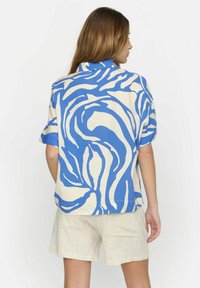 Camicia corta a maniche corte con un motivo astratto blu e crema, realizzata in tessuto leggero, con colletto e un design a vestibilità ampia.