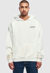 Biały bawełniany hoodie z przednią kieszenią i czarnym napisem "UNLIMITED SKILLS." Długie rękawy i luźny krój, w połączeniu z niebieskimi dżinsami.