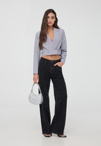 Blazer grigio tagliato con doppi bottoni, abbinato a jeans neri a gamba larga con decorazioni bianche. Accessoriato con una borsa argentata.