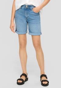 Dżinsowe szorty z jasnym odcieniem, z podwiniętymi nogawkami, dwoma przednimi kieszeniami i zapięciem na guziki z przodu. Połączone z czarnymi sandałami na platformie.