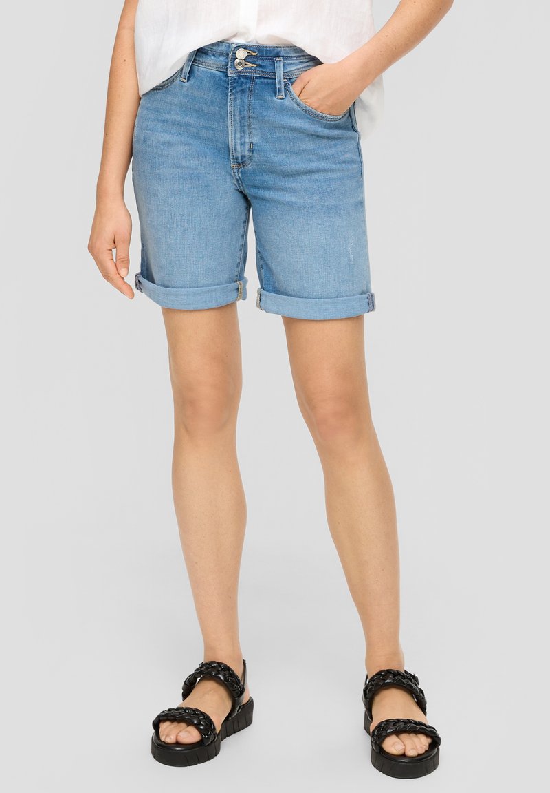 Dżinsowe szorty z jasnym odcieniem, z podwiniętymi nogawkami, dwoma przednimi kieszeniami i zapięciem na guziki z przodu. Połączone z czarnymi sandałami na platformie.