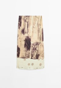 Jupe longueur genou avec motifs abstraits beige et marron, avec coutures verticales et un ourlet plus clair orné de motifs circulaires.