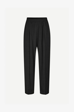 Črne hlače s sproščenim krojem, ki imajo guban sprednji del, elastičen pas in gladko teksturo tkanine. Se končajo pri gležnjih.