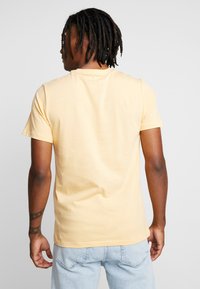 Camiseta amarilla de manga corta con cuello redondo, fabricada en un tejido suave, con un corte relajado y un diseño sencillo, combinada con jeans de mezclilla azul claro.