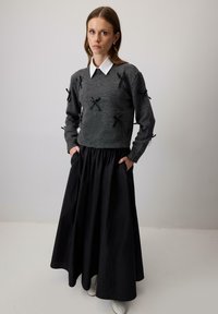 Grijze gebreide trui met zwarte lintaccenten. Gecombineerd met een lange zwarte rok met een getailleerde taille. Witte blouse met kraag eronder.