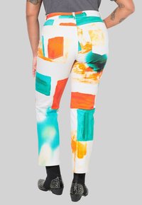 Jeans coloridos y texturizados con patrones abstractos en naranja, azul verdoso y blanco. Diseño ajustado con estilo de cinco bolsillos y detalles cosidos.