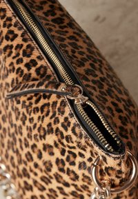 Luipaardprint clutch bag met een gouden rits, faux bont textuur en een metalen ringaccent. Het ontwerp heeft zwarte afwerking en verschillende vlekpatronen.