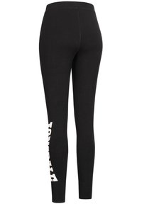 Svarta högmidjade leggings med vit, fet vertikal text på nedre vänstra benet, formsydd stil mot en vit bakgrund.