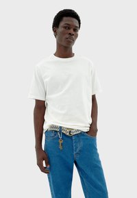 Camiseta blanca de algodón con mangas cortas, combinada con jeans de mezclilla azul; incluye un cinturón tejido con una hebilla metálica y un acento de llavero.