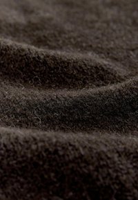 Brunt uldstof med en blød, fnugget tekstur, der har subtile farve- og lysvariationer, arrangeret i bølgende folder.