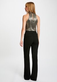 Top sin mangas metálico y brillante con un alto escote y detalle de llave, combinado con pantalones acampanados negros con bolsillos traseros.