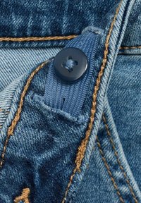 Denim tkanina u različitim plavim nijansama s teksturiranom površinom, s tamnim gumbom, kontrastnim smešnim šavovima i detaljem rupice za gumb.