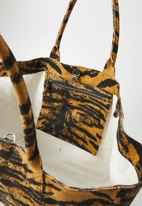Canvas-Tote mit einem Tigerstreifenmuster in Orange und Schwarz. Verfügt über eine Innentasche mit Reißverschluss, lange Tragegriffe und ein geräumiges weißes Innenfach.