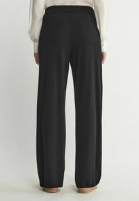 Svarta vida byxor i mjukt tyg, med en platt midja och en slät, flödande design. Avslutet har en subtil finish.