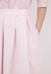 Gonna plissettata rosa chiaro con una texture liscia e una cintura larga. Presenta tasche laterali e una silhouette fluida.