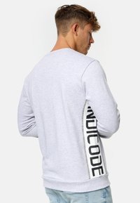 Sweatshirt gris clair à manches longues avec col rond, arborant un logo sur la couture latérale en noir ; matière en mélange de coton avec une texture douce.
