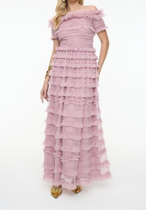 Vrouw draagt een roze, floor-length jurk met blote schouders, gelaagde ruches en goudversierde puntige schoenen.