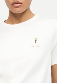 Κοντινό πλάνο προσώπου που φορά λευκή μπλούζα με μικρό σχέδιο πιρουνιού που κρατά σπαγγέτι και κείμενο "Η πάστα κάνει τα πάντα καλύτερα."