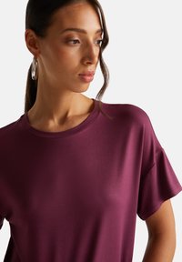 Krátký rukáv fialový top s kulatým výstřihem a hladkým, mírně lesklým materiálem; jednoduchý, čistý design bez vzorů nebo ozdob.