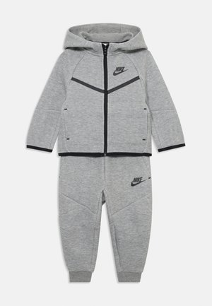 Chándal gris de Nike que incluye una sudadera con cremallera y un logo negro, detalles en negro que contrastan y pantalones de chándal acolchados a juego. Tejido suave.