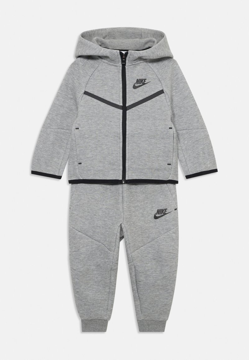 Nike sivi trenirka koja uključuje duksericu sa zipom i crnim logotipom, kontrastnim crnim detaljima i uskim trenerkama. Mekani materijal.