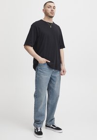 Must lühikeste varrukatega T-särk, mida kannavad helesinised sirgete sääreosadega teksapüksid ja mustad tennised, millel on tekstuuriga pind ja lõdvestunud lõige.