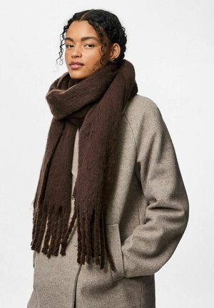 Bufanda marrón de gran tamaño hecha de una tela suave y texturizada, con flecos largos. Llevada sobre el cuello, complementando un abrigo gris.