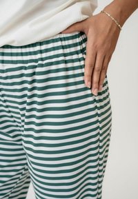 Zelene i bijele prugaste hlače sa rebrastom teksturom, s opuštenim pojasom i rukom koja počiva na strani blizu džepa.