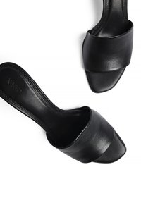 Des sandales noires à enfiler avec une finition en cuir lisse, une large bride supérieure, un bout ouvert et un avant de forme carrée. Détails de coutures subtiles visibles.