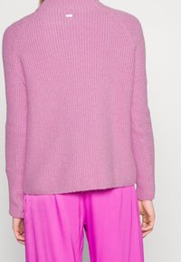 Pull rose tricoté avec un design côtelé texturé, doté d'un col montant et d'un logo à l'arrière, associé à un pantalon rose vif.