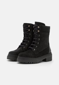 Botas de tornozelo em camurça preta com sola de borracha robusta, bico redondo e ilhós de metal com atacadores. Detalhes nos painéis laterais adicionam textura.