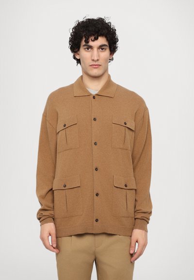 Brun strikket cardigan med krave, der har to brystlommer og knaplukning, parret med beige bukser. Tekstureret stof.