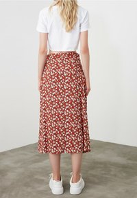 Jupe midi rouge à fleurs blanches, coupe ample et design fluide. Associée à un t-shirt court blanc et des baskets blanches.