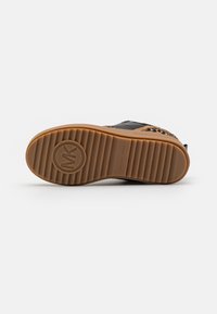 Semelle de chaussure avec une bande de roulement en caoutchouc marron présentant un logo circulaire et un motif rainuré, partie visible de la tige noire et à imprimé léopard.
