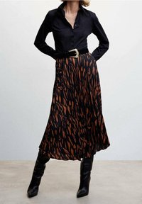 Camisa negra de manga larga combinada con una falda larga hasta el tobillo que presenta un patrón abstracto en marrón y negro, ajustada con un cinturón ancho y botas altas hasta la rodilla.